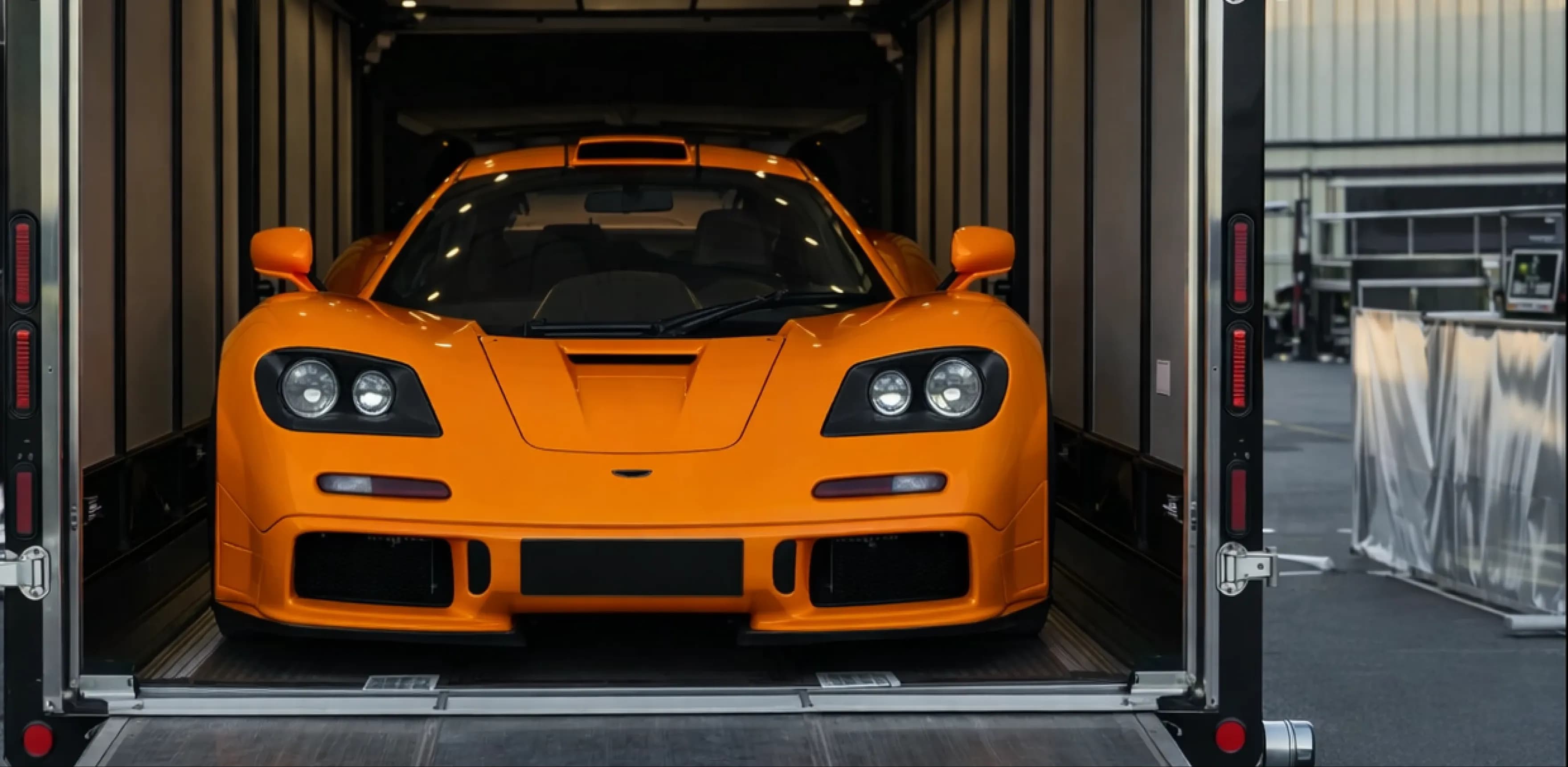 Orange McLaren F1 secured inside enclosed luxury car transport trailer